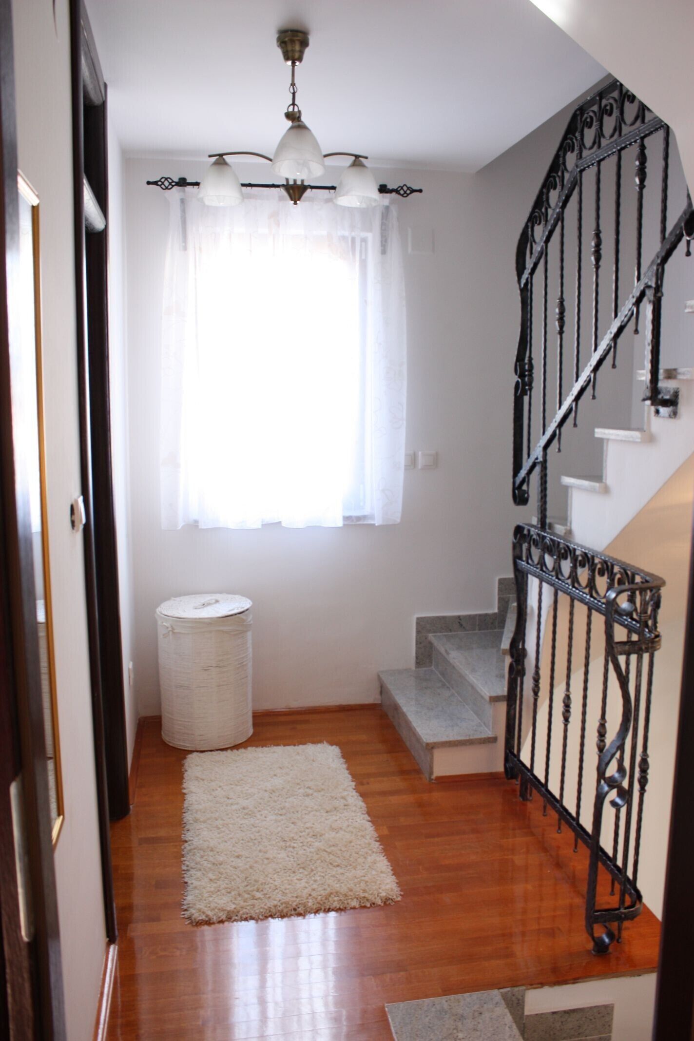 Un escalier avec une rampe en métal noir, un tapis blanc sur le sol et un mur blanc avec une fenêtre et des rideaux.