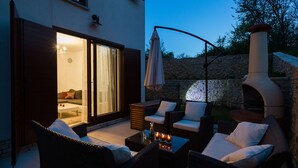 An outdoor patio with wicker furniture, a stone wall, and a pizza oven. - 4 star romantic villa, just a minute walk to the beach, heated pool. (Cizici)