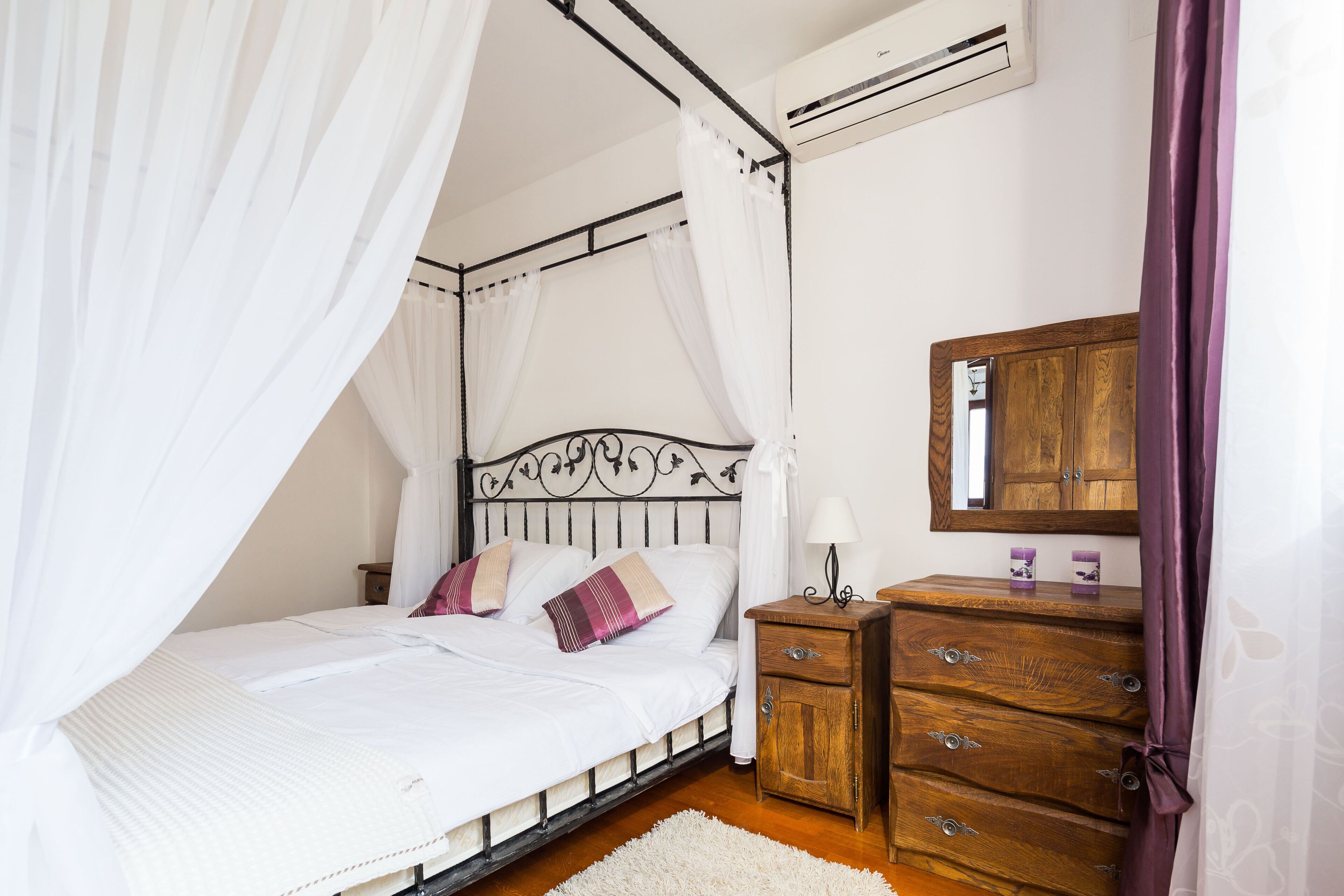 Een slaapkamer met een hemelbed, een houten dressoir en een airconditioning.