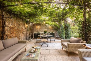 Une terrasse extérieure accueillante, avec des meubles en osier, un mur en briques et une lanterne suspendue.