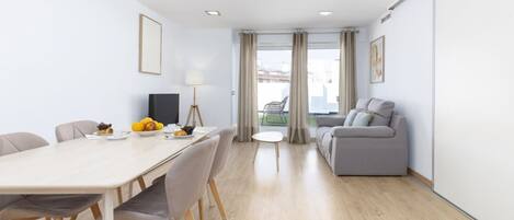 A modern hotel room with a dining area, a sofa, and a view of the city.