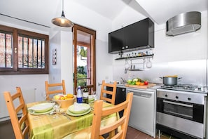 A compact kitchen with a dining table set for two, a built-in oven, and a window with a view of greenery.
