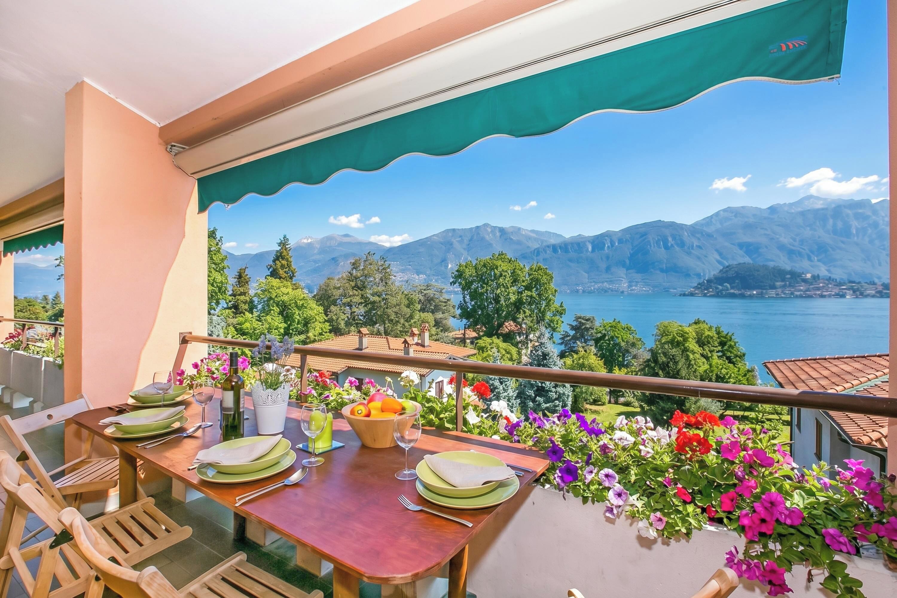 A balcony with a table set for dining, overlooking a lake and mountains.