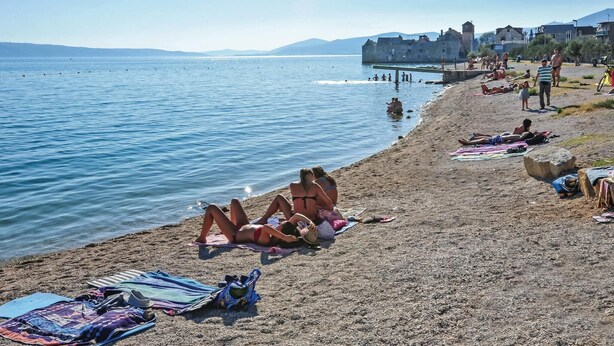 A beach with people sunbathing and swimming, a stone building in the background, and a clear sky. - Amazing home in Kastel Sucurac (Kastel Sucurac)