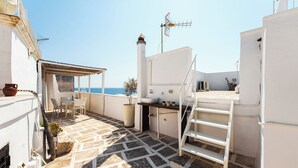 A rooftop terrace with a table and chairs, a potted plant, a white staircase, and a view of the sea. - Casa Conchiglia: Authentic Seafront Apartment (Monopoli)