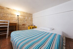 A bedroom with a bed, a chair, a nightstand, a lamp, and a stone wall. - Casa Conchiglia: Authentic Seafront Apartment (Monopoli)