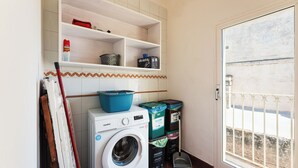 A laundry room with a washing machine, shelves with storage bins, and a door leading to an outdoor area. - Casa Conchiglia: Authentic Seafront Apartment (Monopoli)