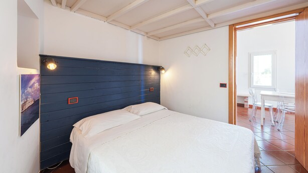 A room with a bed, a wall-mounted light fixture, and a view of the outside. - Casa Conchiglia: Authentic Seafront Apartment (Monopoli)