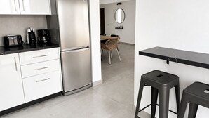 Moderni keittiö, jossa on ruostumattomasta teräksestä valmistettu jääkaappi, valkoiset kaapit, kahvinkeitin sekä ruokailutila, jossa on tuoli ja pöytä.
