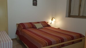 Una cama individual con una colcha a rayas, una mesita de noche con lámpara y un pequeño banco.