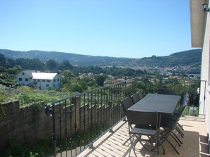 A balcony with a table and chairs, overlooking a town with houses and hills in the distance. - COUNTRY HOUSE WITH EXCELLENT MOUNTAIN VIEWS (Cabanas (A Coruna))