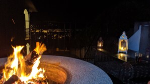 Un foyer avec des flammes, une lanterne et un verre à boire sur une terrasse.