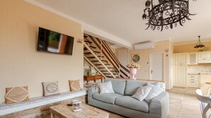Un salon comprenant un canapé, une table basse, un téléviseur fixé au mur, un escalier menant à une autre pièce et un coin cuisine.