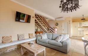 Una sala de estar con sofá, mesa de centro, televisor montado en la pared, escalera que lleva a otra habitación y área de cocina.