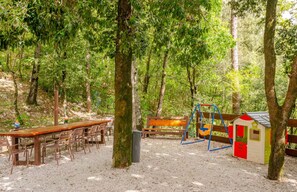 Un área de picnic con una mesa y sillas, un conjunto de columpios y una pequeña casita de juegos.