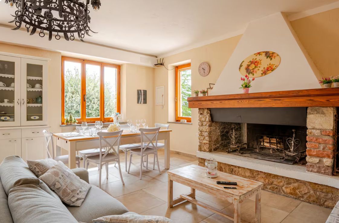 A dining area with a table set for four, a fireplace, and a sofa in a room with large windows.