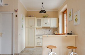 A kitchen with white cabinets, a bar area with stools, and a hanging light fixture.
