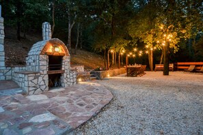 A stone-built outdoor kitchen with a chimney, surrounded by a gravel area and trees. - VillaSubasioRelax, panoramic villa with swimming pool, natural park, Spello, Assisi (Spello PG)