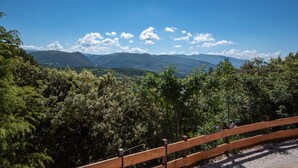 Une clôture en bois surplombe un paysage montagneux, caractérisé par une végétation luxuriante et un ciel bleu clair.