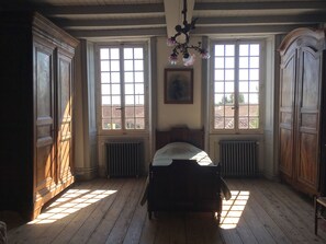 A room with a wooden bed, two windows with shutters, a radiator, and a chandelier. - Holiday rental house with farmyard and garden near Cognac. (Les Métairies)