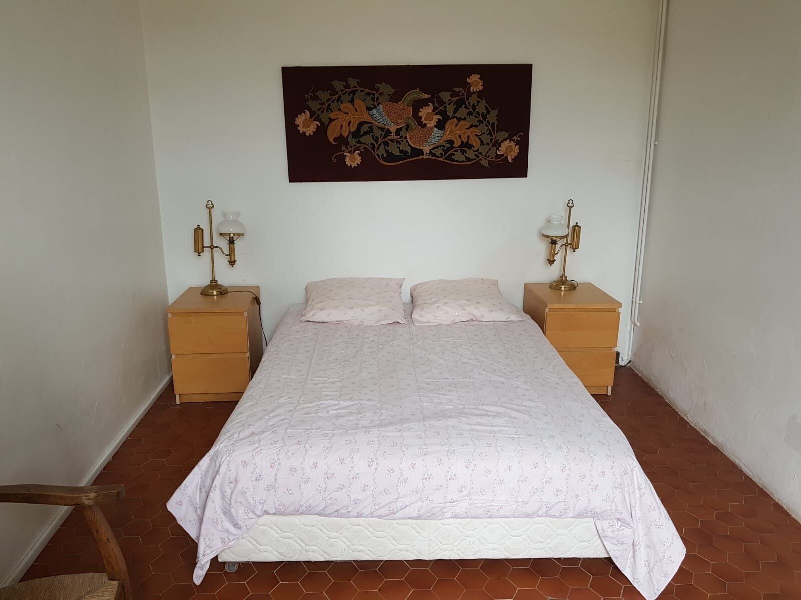 A bedroom with a bed, two nightstands, two lamps, and a wall hanging.
