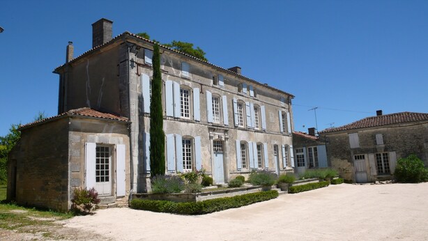 A two-story stone building with a symmetrical facade, multiple windows with shutters, and a central entrance. - Holiday rental house with farmyard and garden near Cognac. (Les Métairies)
