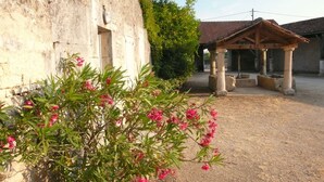 A building with a stone facade, a covered outdoor area with columns, and a garden with pink flowering plants. - Holiday rental house with farmyard and garden near Cognac. (Les Métairies)