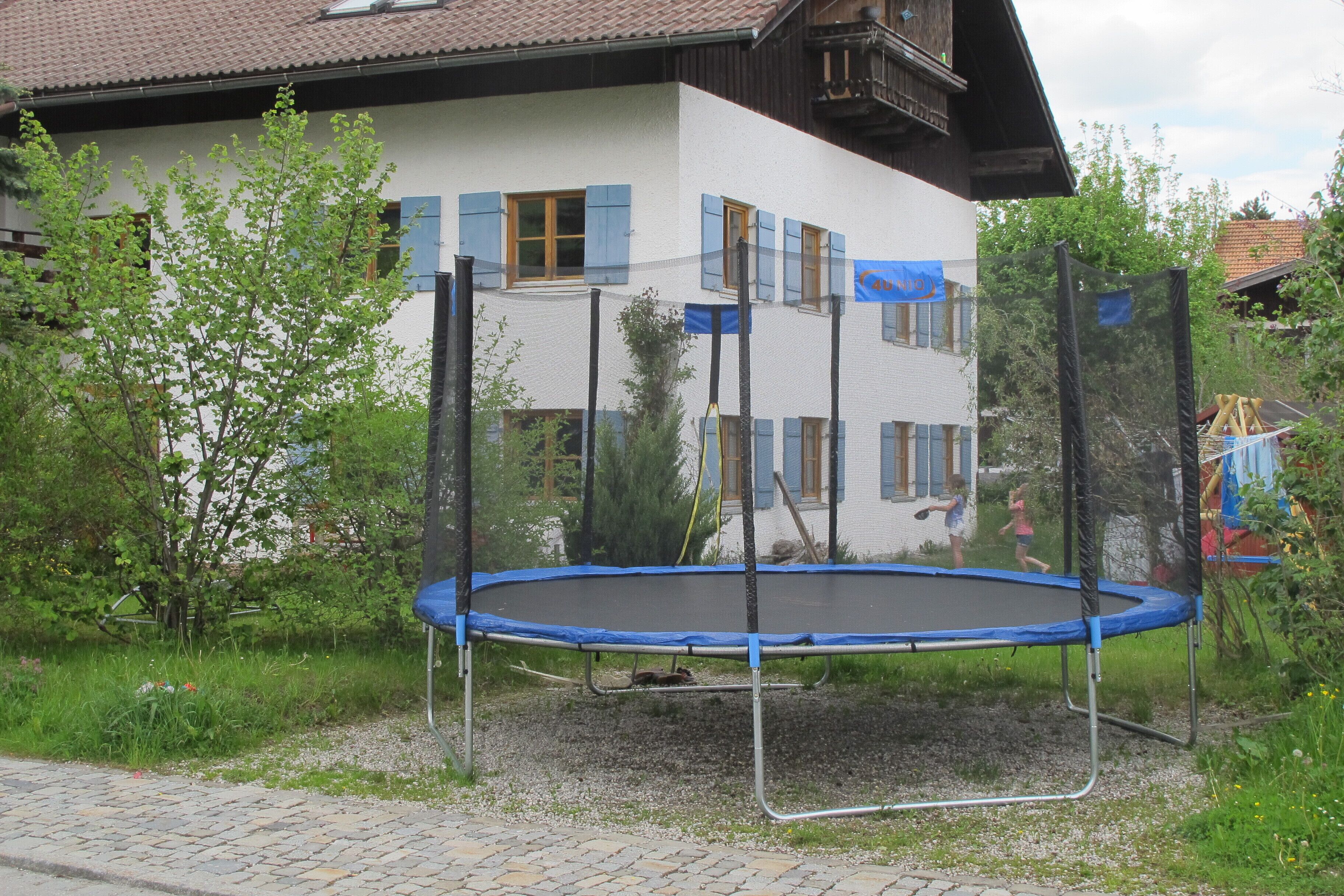 A house with a trampoline in front, surrounded by greenery.