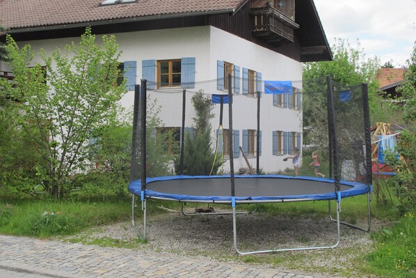 A house with a trampoline in front, surrounded by greenery.