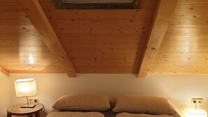 A room with a sloped ceiling, wooden beams, a bed with two pillows, and a bedside table with a lamp. - Close to the mountains! (Pfronten)