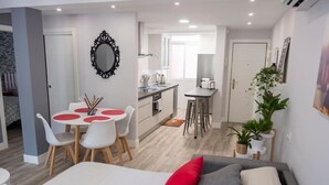 A modern hotel room with a bed, a dining area with a table and chairs, a kitchen area, and a living area with a sofa and a plant. - VALTOUR New apartment Downtown+Wifi+A/C+Terrace (Valladolid)