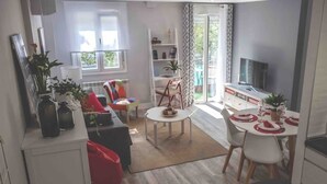 A modern living room with a sofa, a coffee table, and a dining area with a table set for four. There is a bookshelf and a TV in the room. - VALTOUR New apartment Downtown+Wifi+A/C+Terrace (Valladolid)