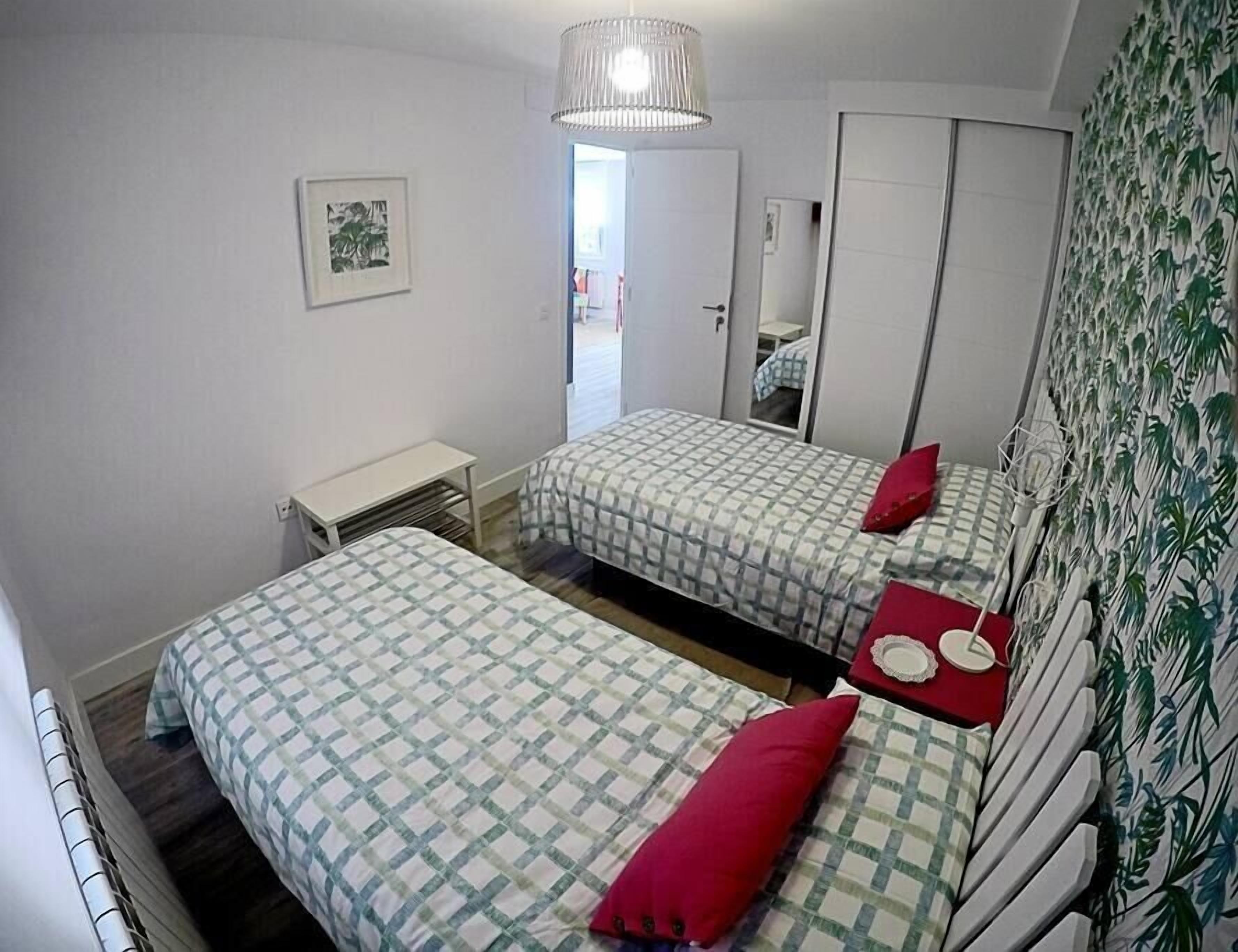 A bedroom with two beds, a small table, a mirror, and a wall with a leaf pattern.