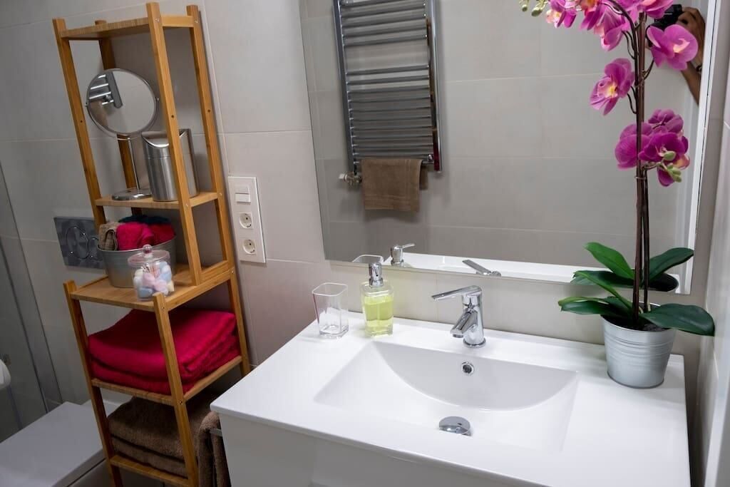 Ein Badezimmer mit einem weißen Waschbecken, einer Holzhilfe mit roten Handtüchern, einem Spiegel und einer Orchidee im Topf.