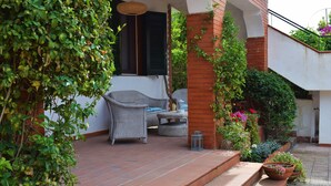 Un espace extérieur aménagé avec des meubles en osier, une colonne en briques et des plantes en pot, le tout abrité.