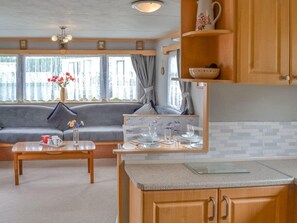 Cocina compacta con armarios de madera, una mesa de comedor y un ventanal con cortinas.