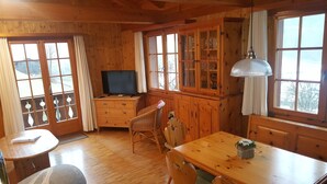 A wooden cabin interior with a dining table, chairs, a television, and a cabinet with glass doors.