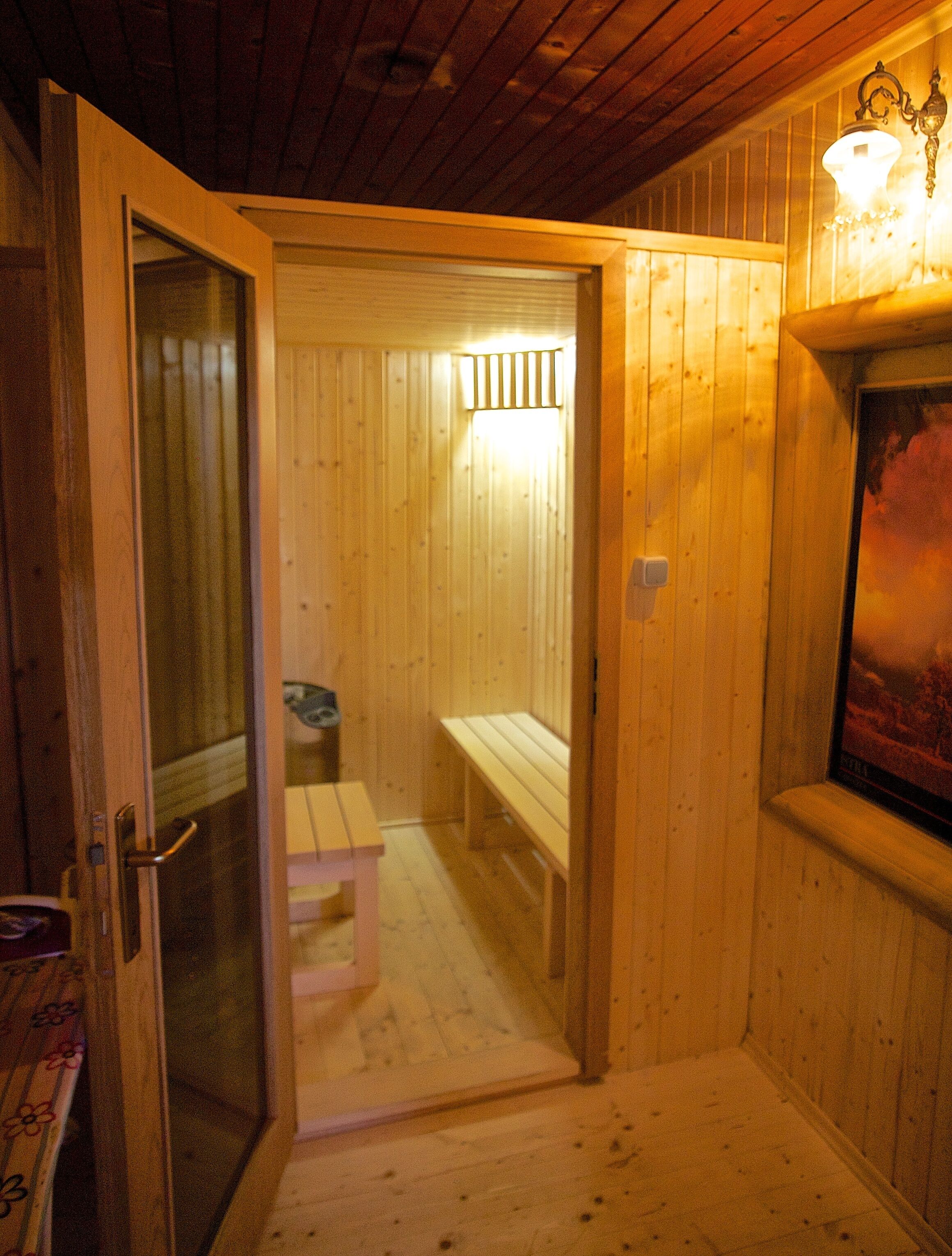 A wooden interior with a bench and a small table, a door leading to another room, and a wall-mounted light fixture.