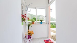 A balcony with a view of a bridge and hills, a coat rack with a potted plant, and a colorful mat on the floor. - Stunning home in Plat (Plat)