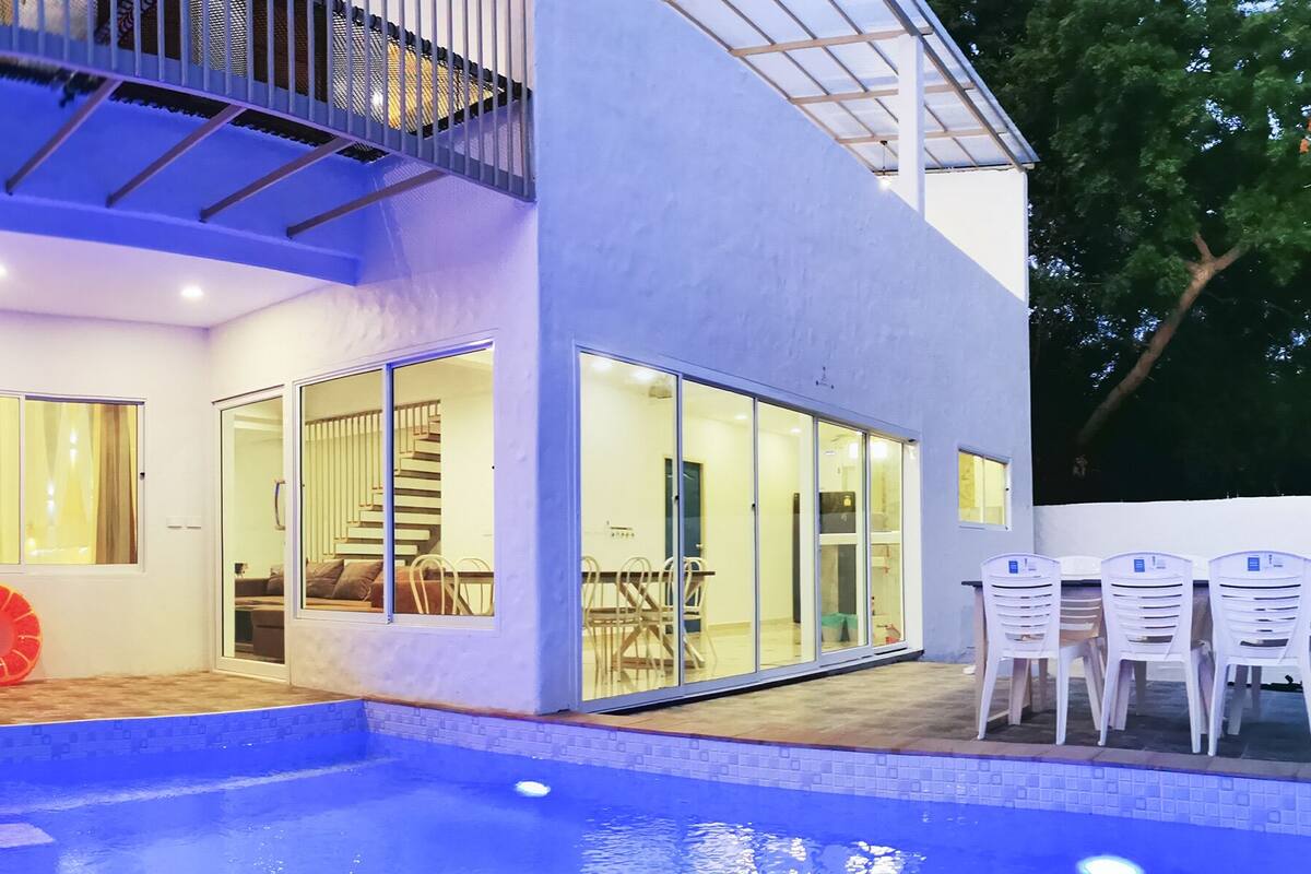 Een modern huis met een zwembad, grote glazen deuren en een trap naar een balkon.