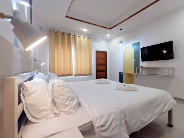 A modern hotel room with a large bed, a flat-screen TV mounted on the wall, and a window with curtains.