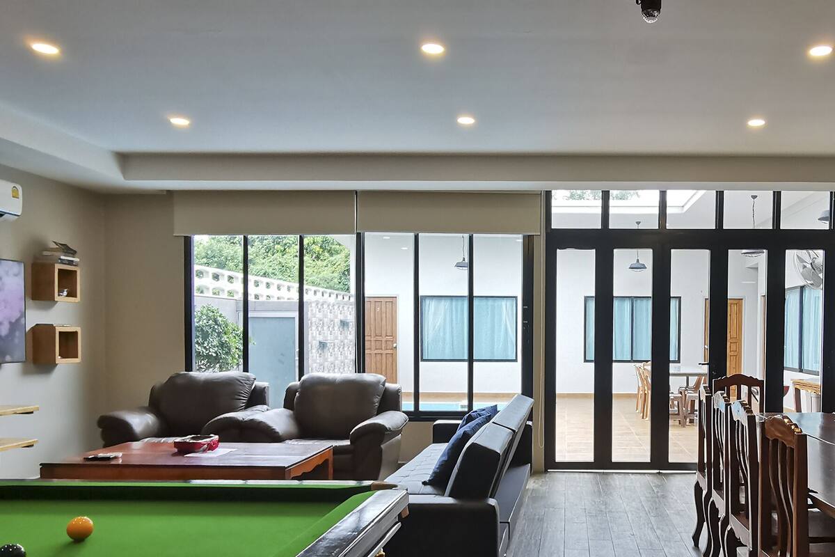Een moderne woonkamer met een pooltafel, leren banken en een eetgedeelte met houten meubels.