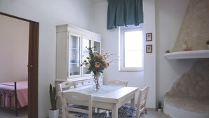 Ein Essbereich mit einem weißen Tisch, Stühlen, einer Blumenvase, einem Schrank und einem Kamin.