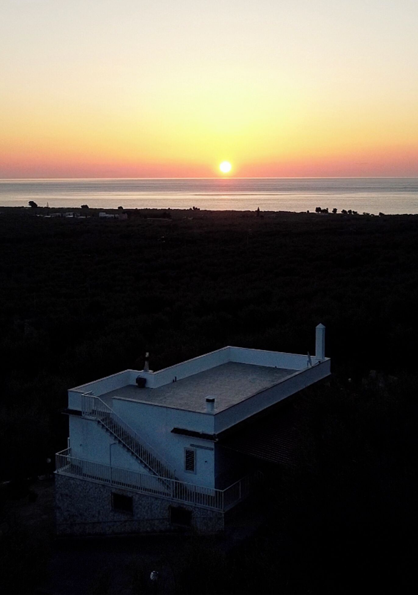 Un bâtiment doté d’un toit plat et d’un escalier menant à un balcon, situé près d’une étendue d’eau au moment du coucher du soleil.
