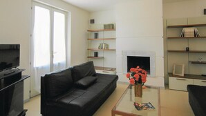 A living room with a black sofa, a glass coffee table with a magazine, a fireplace, and bookshelves. - Lovely home in Torre del Lago Puccini (Torre del Lago Puccini)