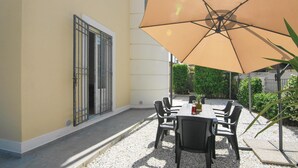 An outdoor patio with a table and chairs under a large umbrella, surrounded by gravel and greenery. - Lovely home in Torre del Lago Puccini (Torre del Lago Puccini)