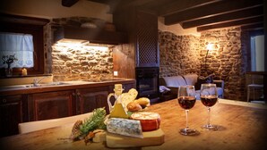 Une cuisine chaleureuse avec des murs en pierre, des armoires en bois et une cheminée en pierre. On peut voir deux verres de vin rouge posés sur le comptoir.
