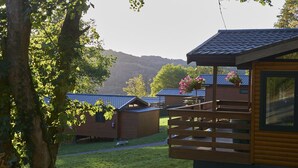 Une rangée de chalets en bois dotés d’un balcon, entourés de verdure et avec une chaîne de montagnes en arrière-plan.
