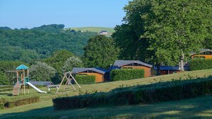 Un cadre rural avec une structure de jeux en bois, une balançoire et un petit bâtiment doté d’un toit en pente.