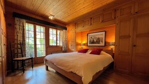 Ein Zimmer mit Holzwänden, einem großen Bett, einem Sessel und einem Fenster mit Vorhängen.
